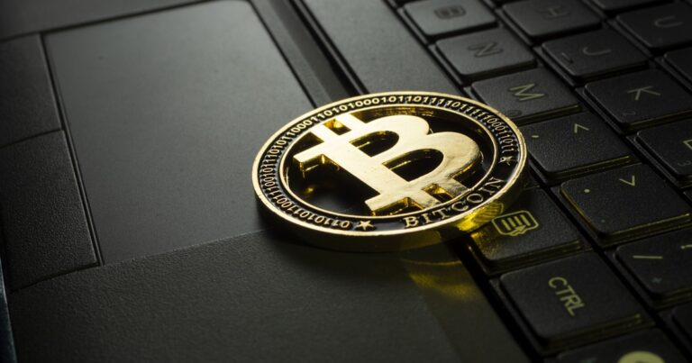 Gold Bitcoin coin on laptop keyboard representing buying cryptocurrency for the first time