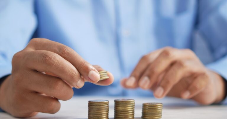 Person stacking gold coins representing consistent dollar cost averaging into dividend stocks