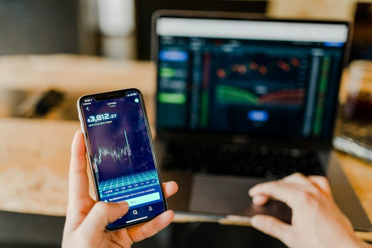Hand holding smartphone displaying stock trading charts representing DRIP stock dividend reinvestment plan investing